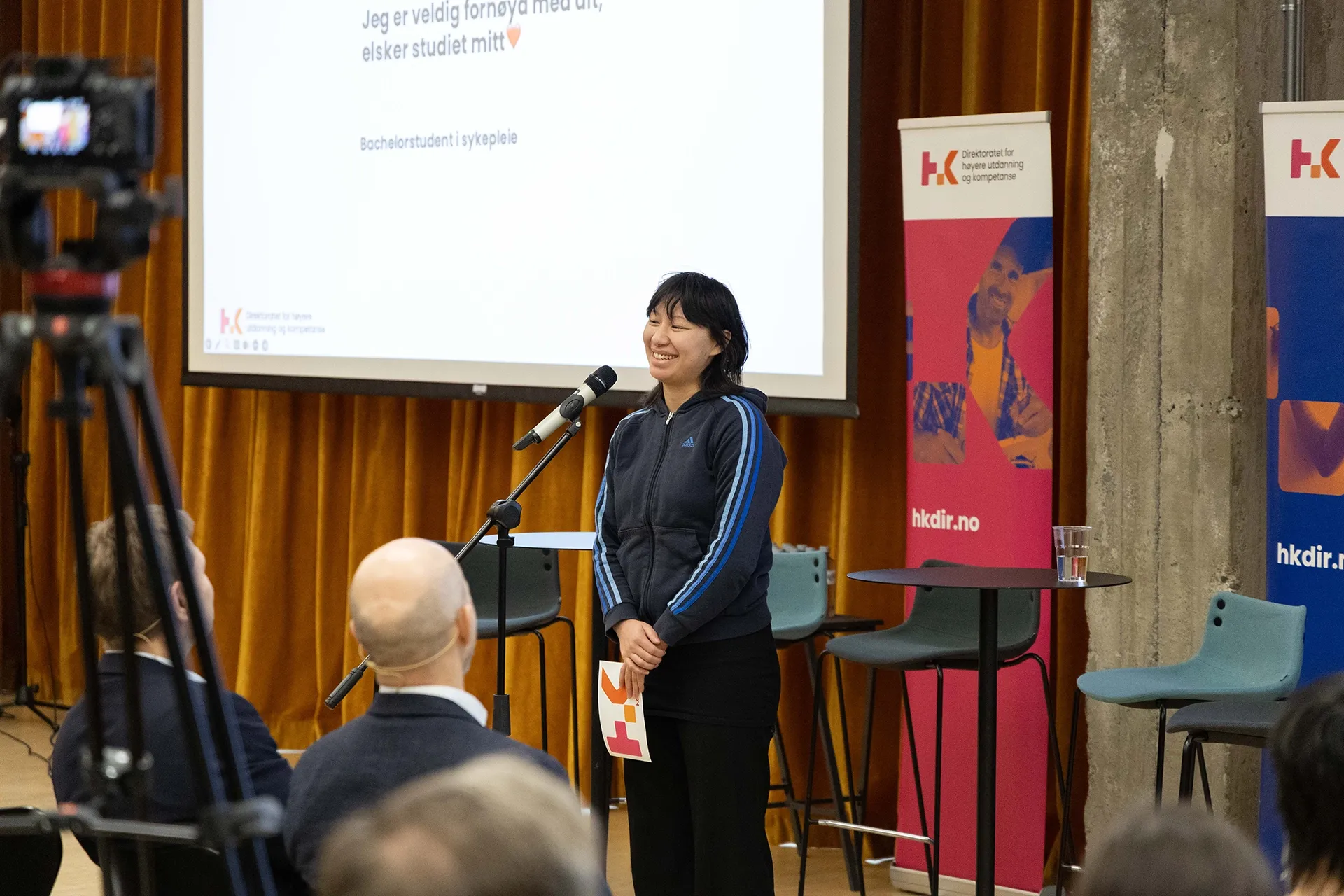Kvinnelig student smiler mens hun presenterer foran et publikum