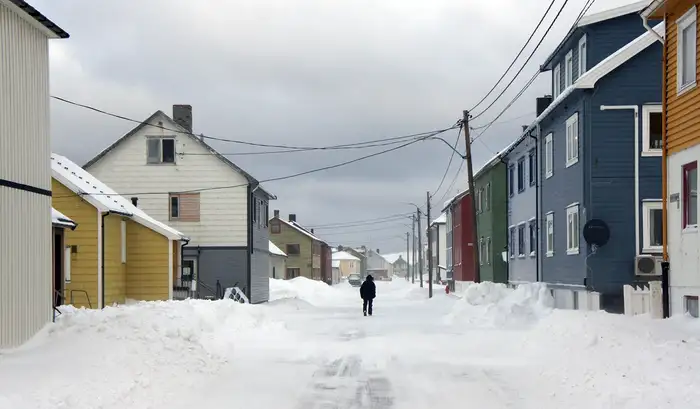 En snøfylt gate med hus på begge sider, en mann går i gata 