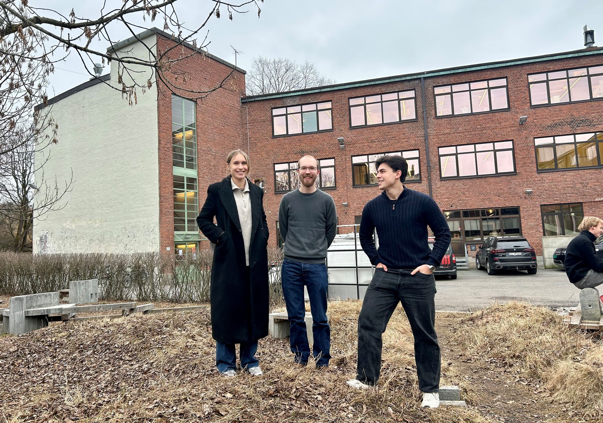 Tre designere oppstilt foran en musrsteinsbygning. 