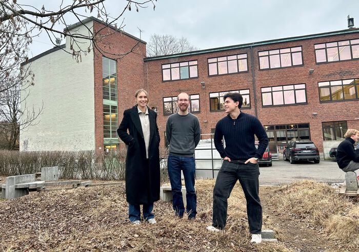 Tre designere oppstilt foran en musrsteinsbygning. 