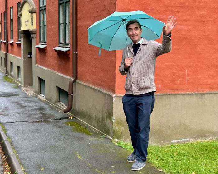 Mann med paraply. Står foran rødt hus.